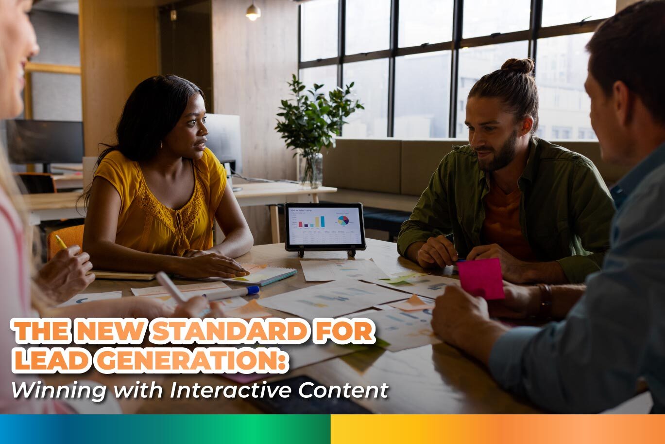 A diverse team of four professionals collaborating around a table covered with charts and documents, with a tablet displaying data analytics in the center.